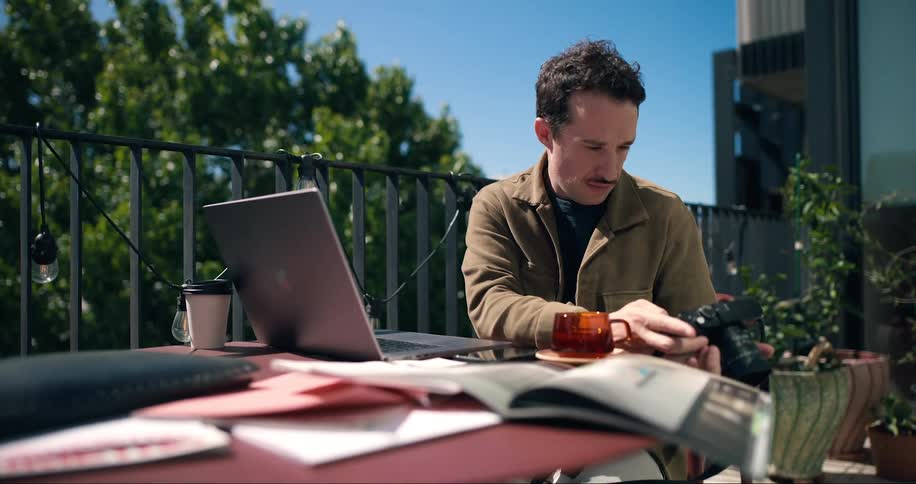 A clip of a man typing on a computer and also checking a camera