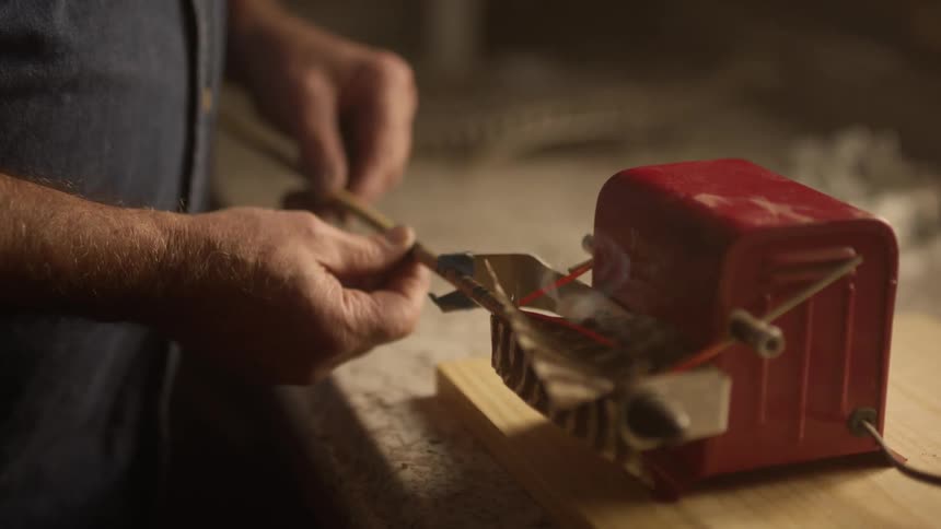 Hand holding an arrow and cutting the feather on a small red machine