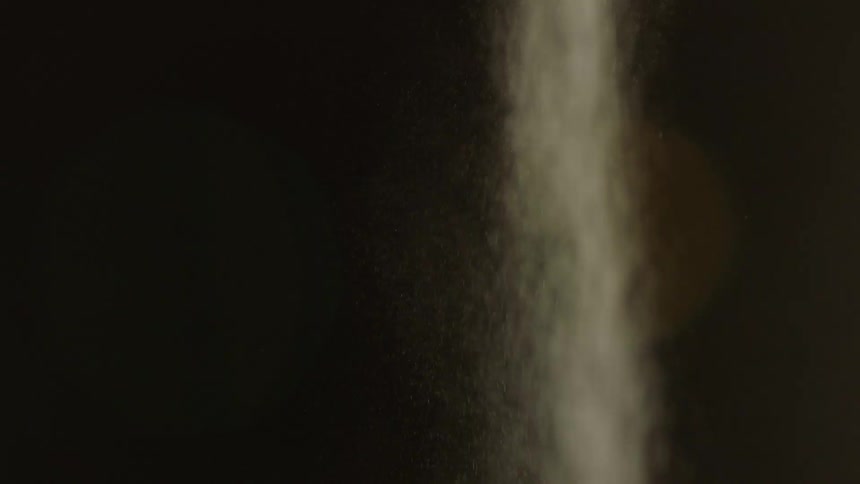 Closeup of white sand or dust cascading against a dark backdrop