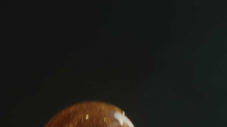 Closeup of a goldenhued molten glass sphere being shaped with a metal tool