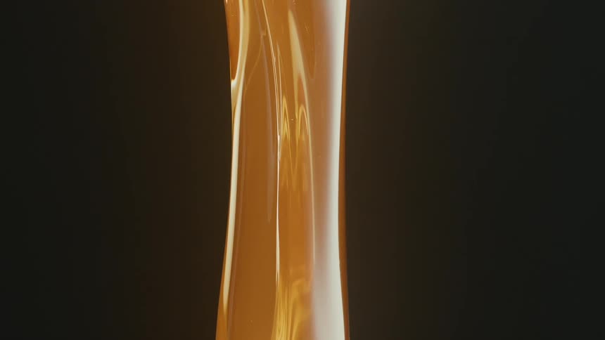 A thick strand of golden caramel falls its viscous texture highlighted against a dark background