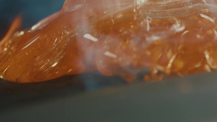 Molten glass over a piece of wood burning from the intense heat with flames and smoke rising