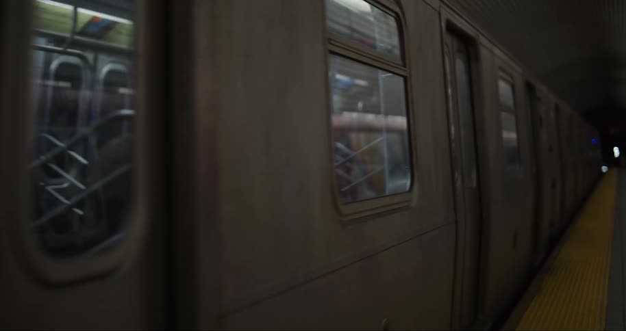 A train car with closed doors is seen from a slightly elevated platform leaving the station with a glimpse of a person sitting inside