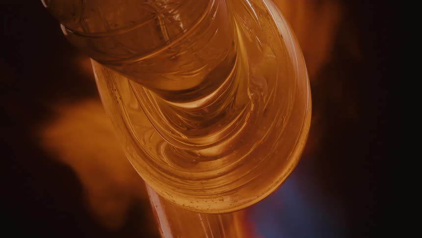 A piece of molten glass is being shaped with fire capturing the glassblowing process