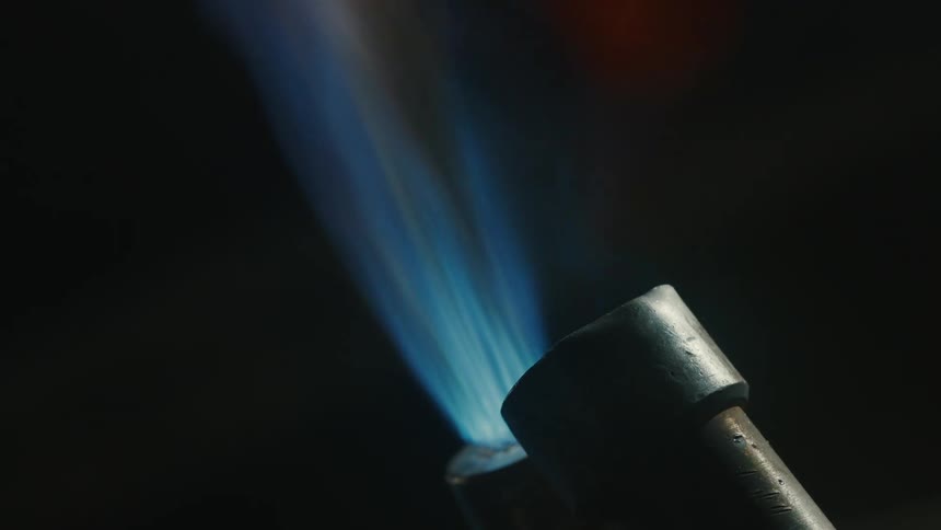 Closeup of a blowtorch nozzle with a flame burning against a dark background