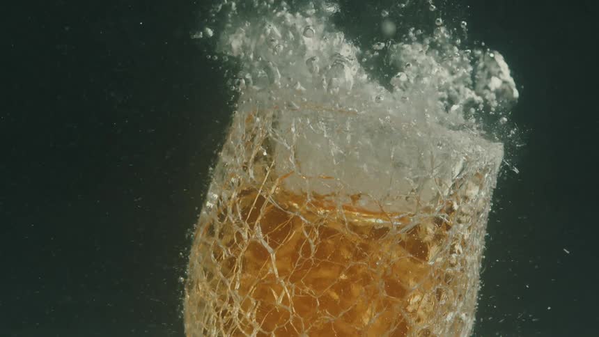 A hot piece of solid glass is submerged in water creating a splash of bubbles and cracking against a dark background