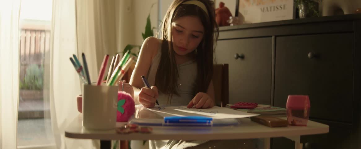 Young girl sitting at her desk in her room drawing with markers on paper
