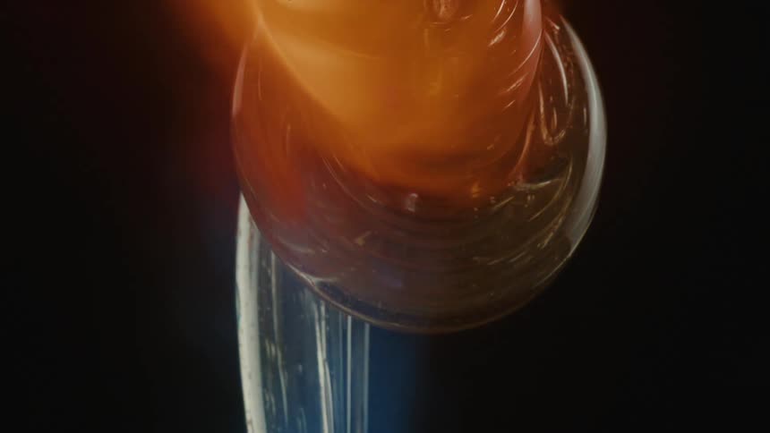 A blob of glass is being heated by an open red flame capturing the glassblowing process