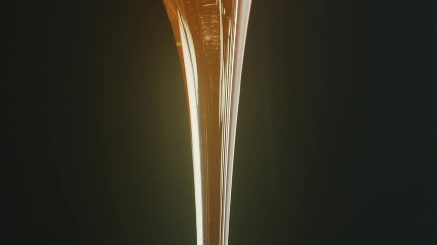 A viscous transparent blob of molten glass is being stretched vertically against a dark background