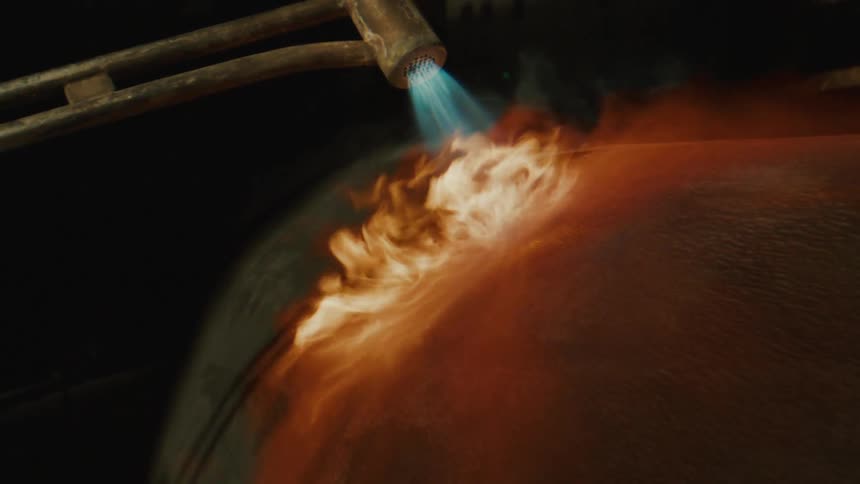 A flame torch fires onto a metallic cylinder creating a swirl of orange and yellow sparks against a dark backdrop
