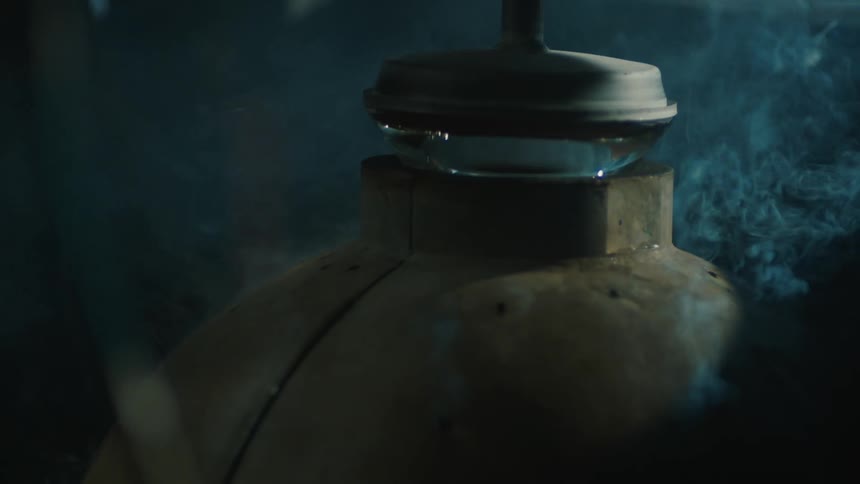 Closeup of a metal container with a glass valve on top surrounded by steam in a dark environment