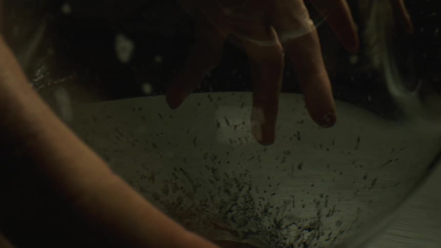 A pair of hands holds a glass jar over a rotating table for sanding its base
