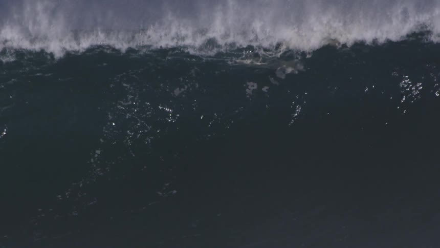 A large wave is breaking as a surfer rides the wave