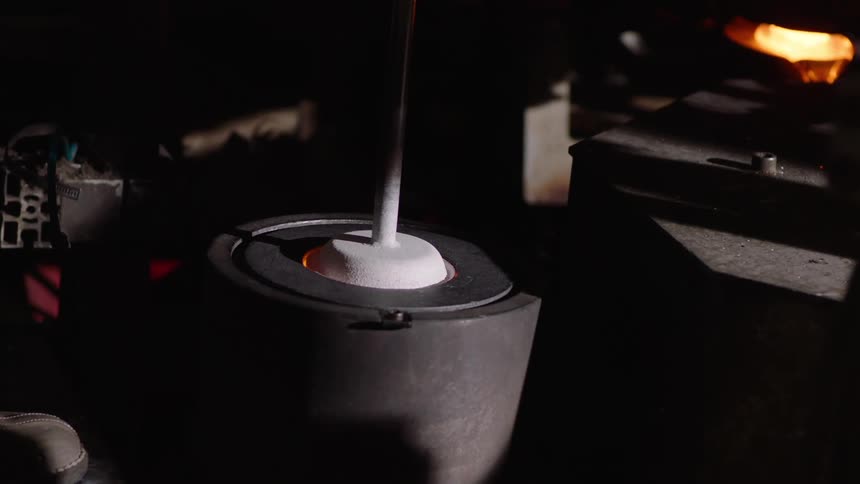 Closeup of an industrial machine shaping molten glass into cylindrical shapes