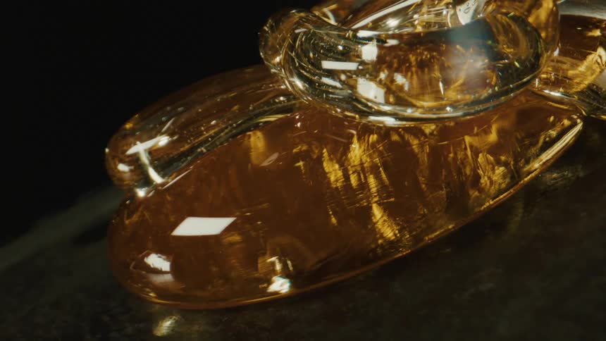 An amber piece of molten glass resting over a surface reflecting light