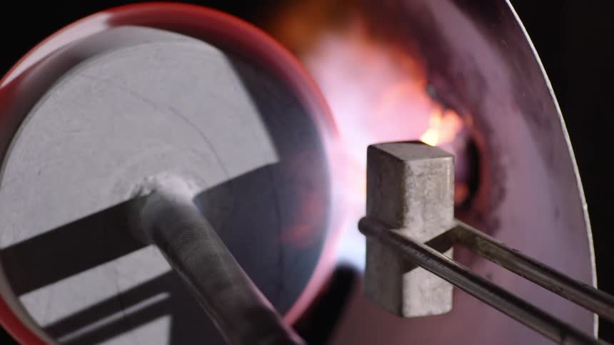 A close up of a glass blowing process where a vase is being heated and shaped inside a furnace