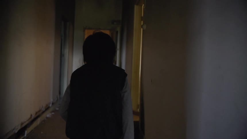A person in a dark vest walks down a white hallway