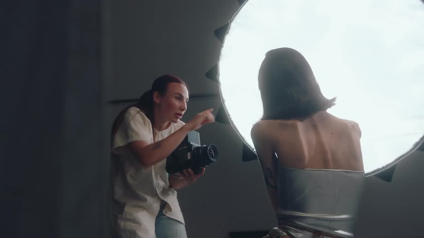 Photographer giving directions and taking photos of a young woman against a studio light