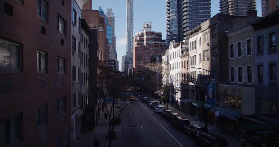 A street in new york city stretches into the distance framed by a mix of older lower brick buildings and modern taller skyscrapers under a bright sky