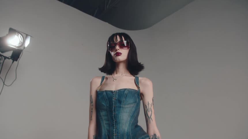 Woman wearing a denim dress and sunglasses taking pictures in a studio