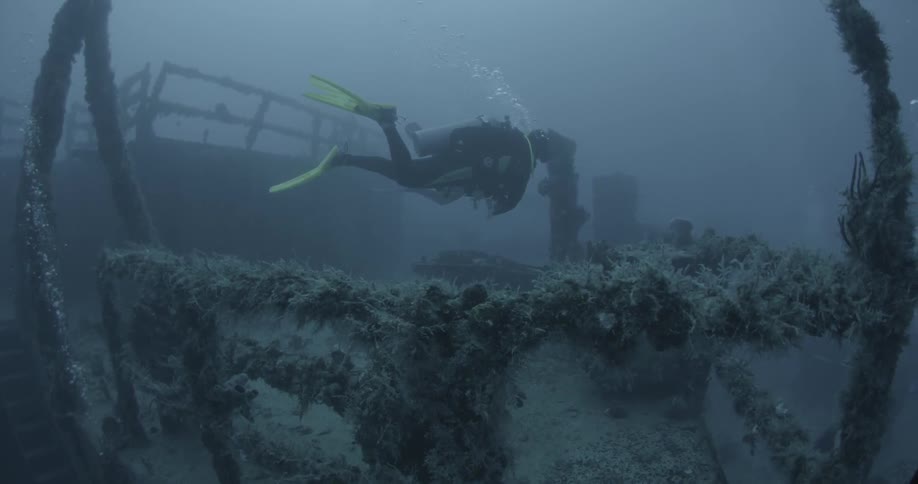 A diver swims near ship wreckage in the ocean