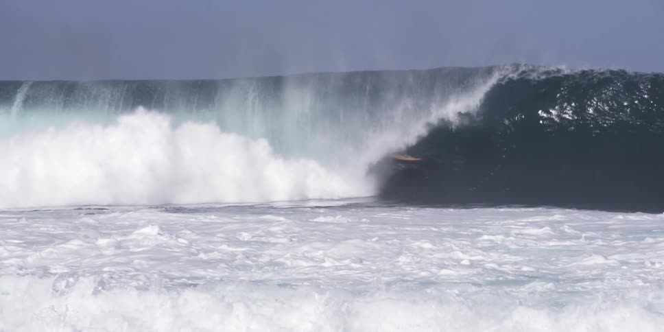 A very tall wave has many surfers on it as it crashes