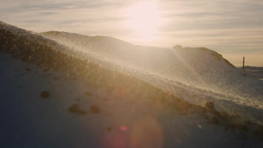 Snow flying down a hill with a reflection of the sun on the horizon