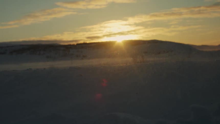 Snow flying between mountains with the sun on the horizon