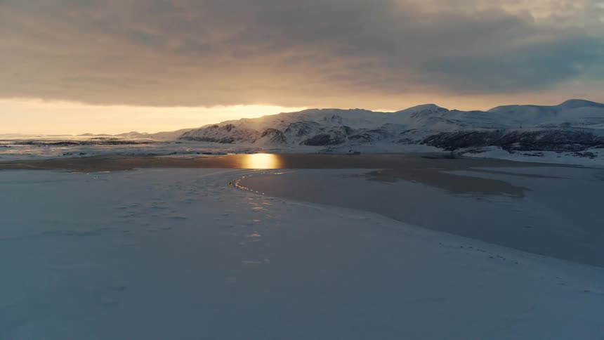 Small lake surrounded by snowcapped mountains and the sun on the horizon