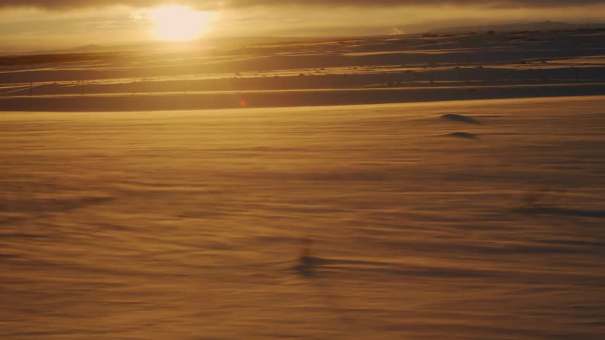 Landscape of a field covered in snow with a sun on the horizon