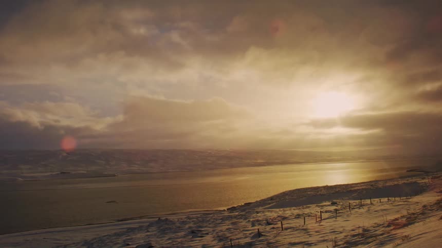 Snowy landscape with lake and sun rising on the horizon