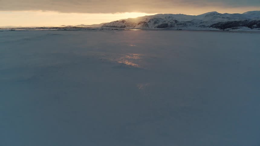 Aerial landscape of a vast snowy field with mountains in the background