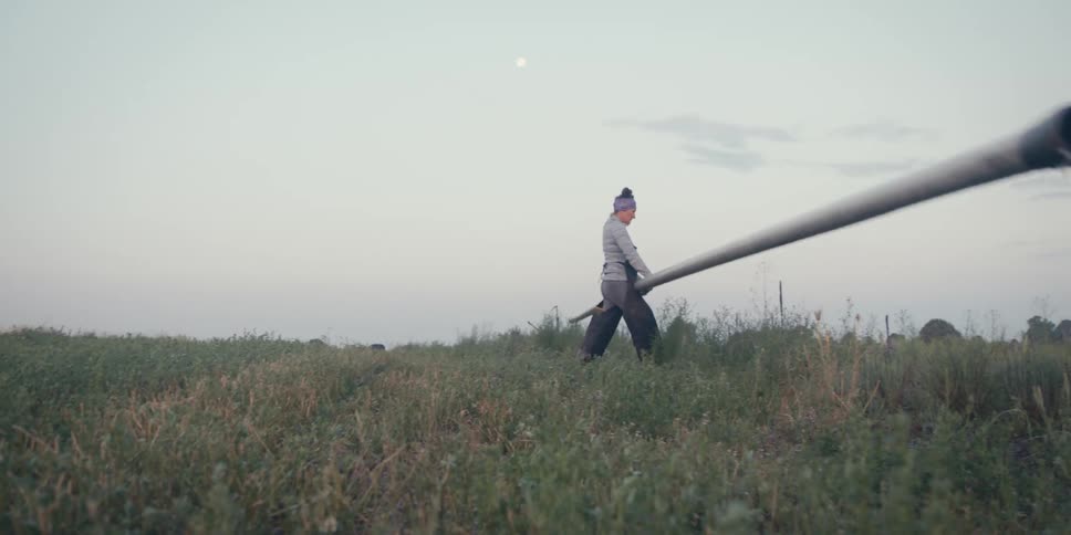 Woman walking in a grassy field and carrying a metal pipe