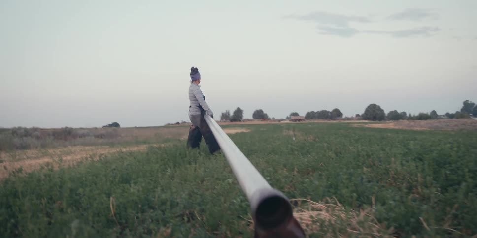 Woman in an agricultural field carrying a metal pipe