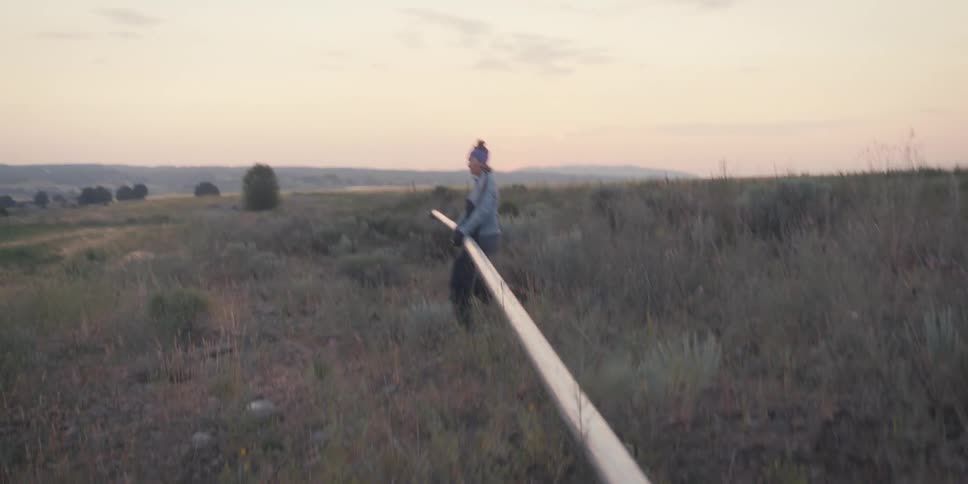 A woman carries a pipe across a field