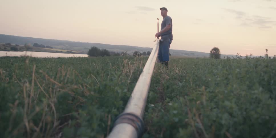 Man carrying and connecting a metal pipe of an irrigation system