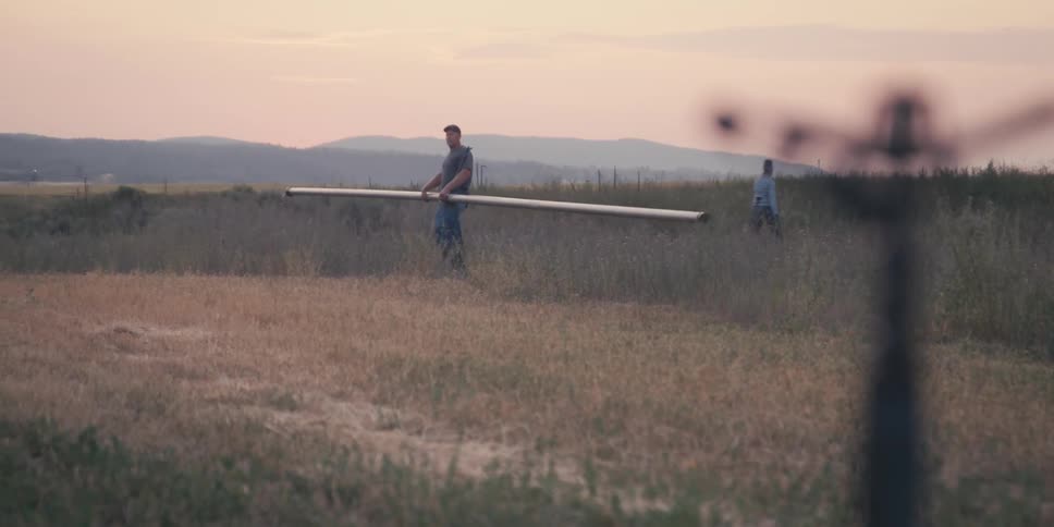 Man walking through a field carrying a metal pipe