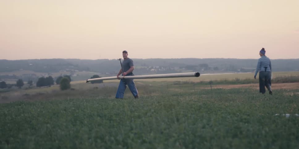 Man in a field carrying a long metal pipe