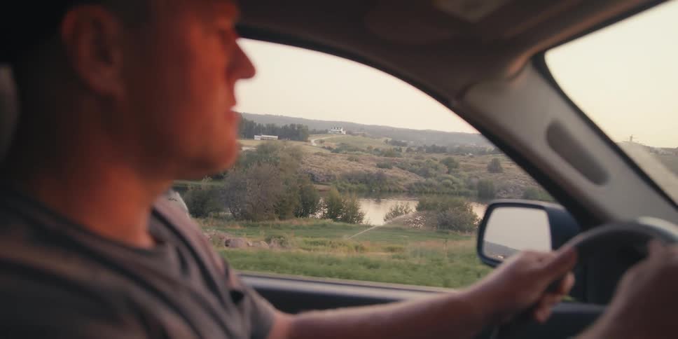 Man driving car through a natural area with a lake in the background