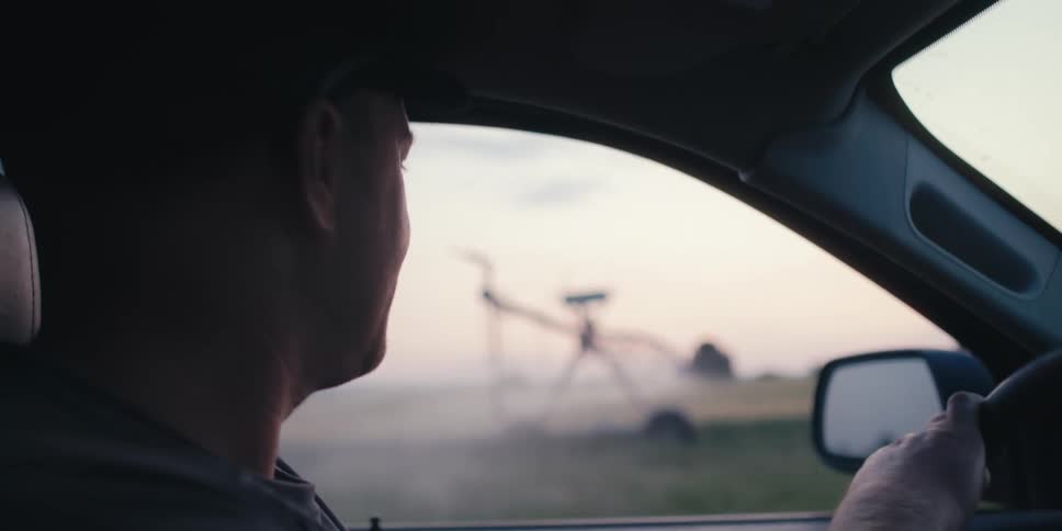 Man driving vehicle and looking at a machine making irrigation system in a rural area