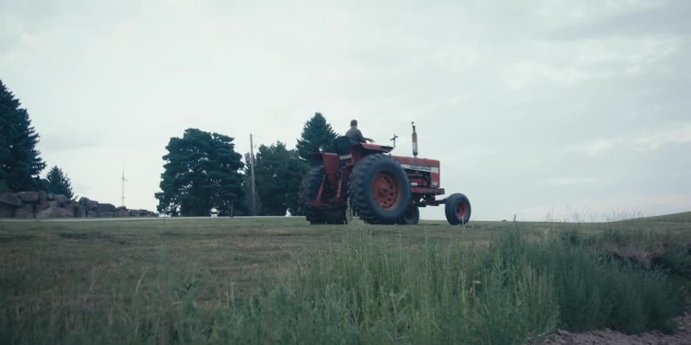 Man driving a tractor through a farm field on a cloudy day