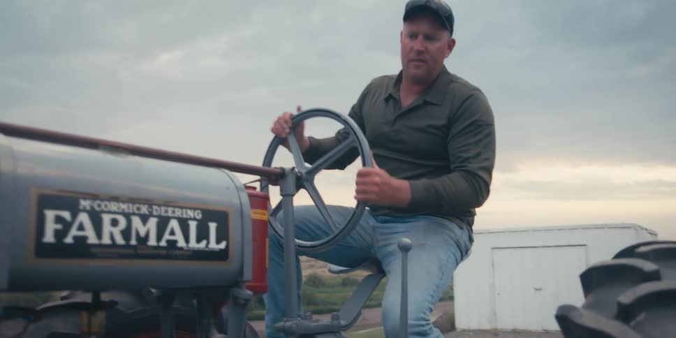 Man in cap turning steering wheel of farm tractor