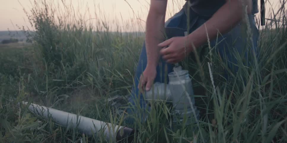 A man turns the water spigot on and carries a pipe