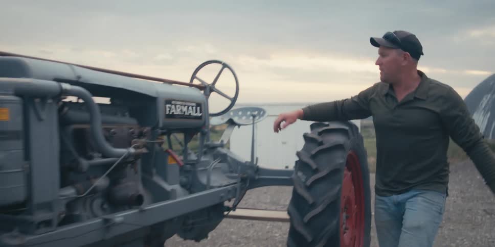 Man getting out from behind the wheel of the tractor and going to check the engine