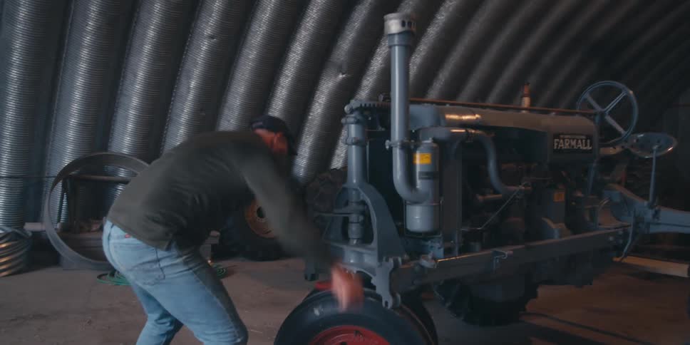 Man with a red tool turning on the engine of a farm tractor