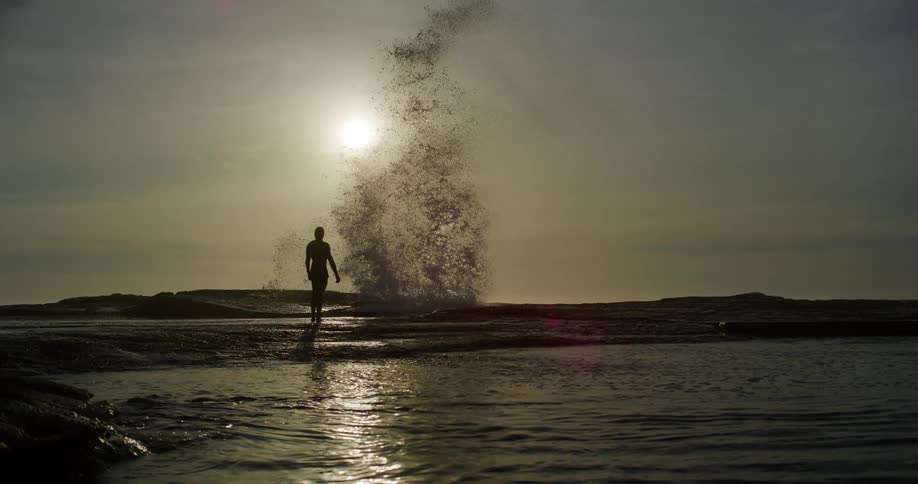 A wave splashes high over a persons head on the beach
