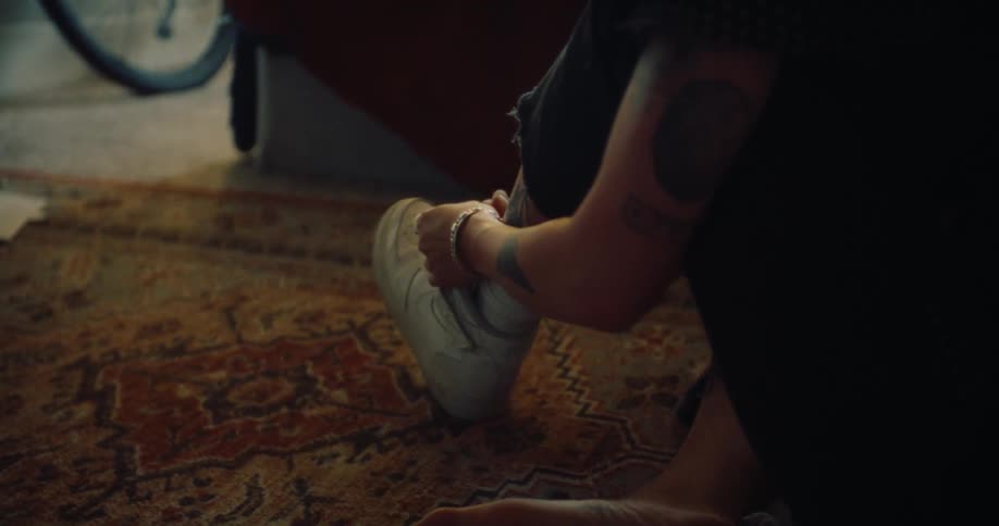 Person sitting on carpet and tying shoelaces on white sneakers