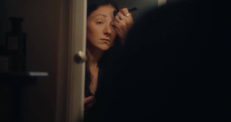 A woman uses a brush to put makeup on in the mirror