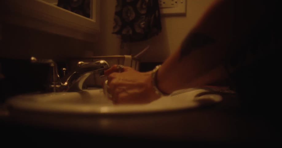 A close up of a woman with tattooed arms washing her hands in the bathroom at home