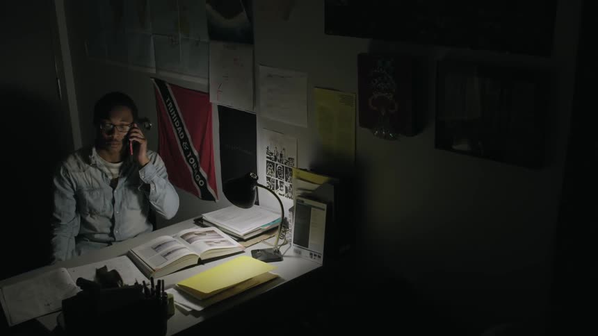 A man talks on the phone in a dimly lit room